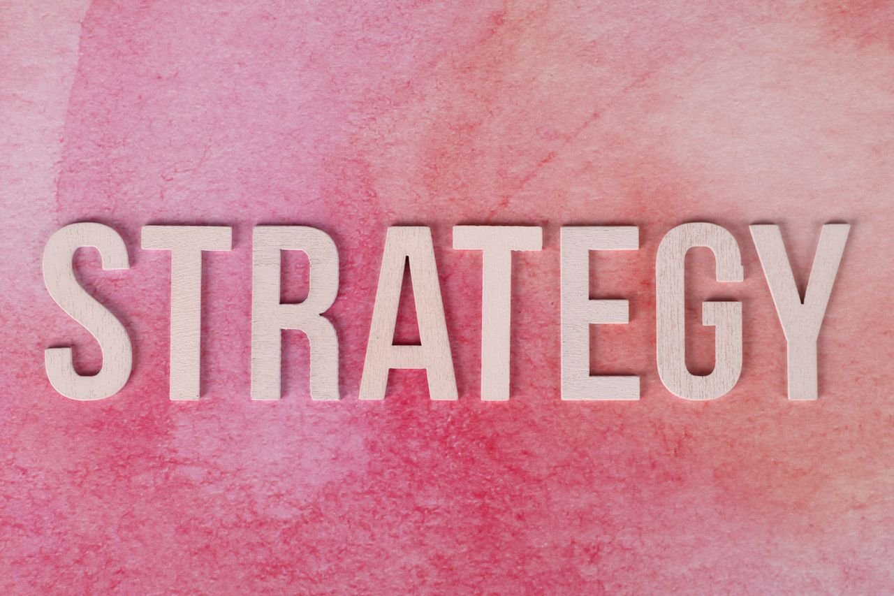 Wooden letters spelling 'Strategy' on a pink textured background.
